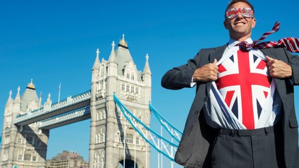 Un homme avec le drapeau britannique sur son t-shirt, sa cravate, ses lunettes devant le Tower bridge